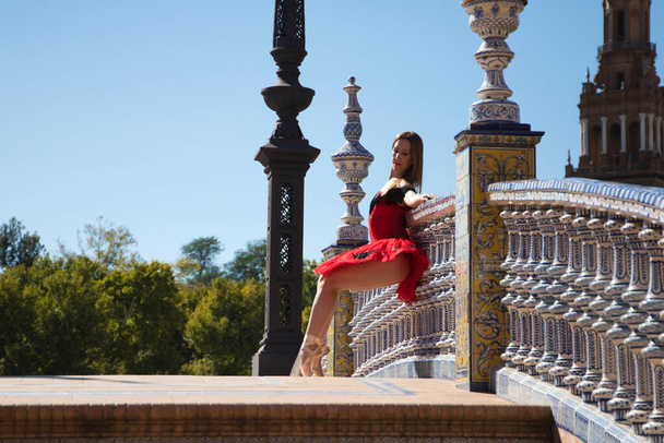 Seville 'deki korkuluklara yaslanmış kırmızı tüyle balerin. Dansçı farklı pozlar verir ve korkuluklara uzanır. Klasik bale konsepti - Fotoğraf, Görsel