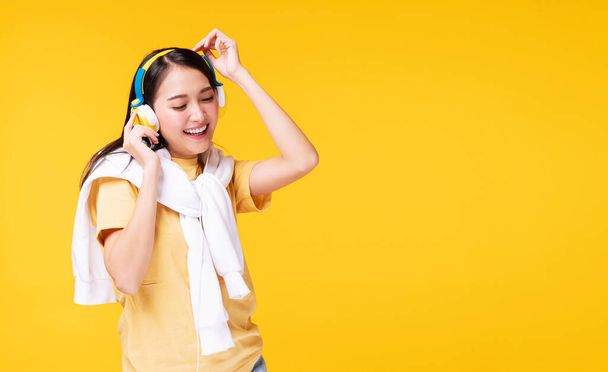 Fröhlich genießen junge Frauen mit Kopfhörern Musik vom Smartphone hören und entspannen sich beim Tanzen vor einsamem gelben Hintergrund. Lifestyle-Freizeit mit Hobby-Konzept. - Foto, Bild