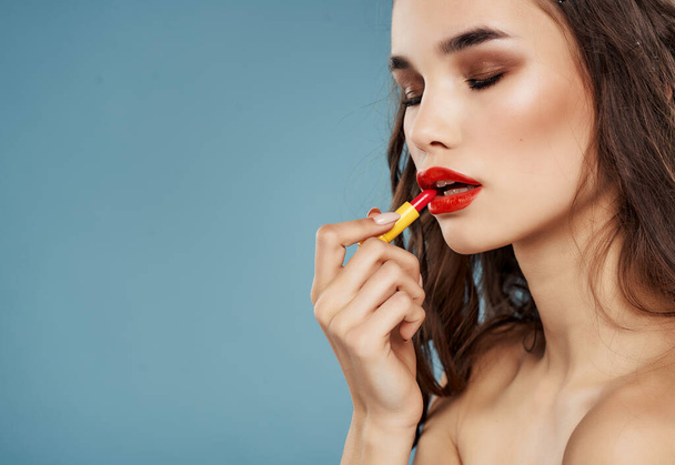 pretty brunette appying  lipstick on  blue background. High quality photo - Photo, Image