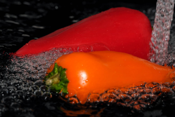 Multicolored bell peppers are washed in clean water close-up macro photography on a black background - Photo, Image