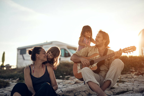 Perhe lomalla, laulamassa, soittamassa musiikkia kitaralla ja nauttimassa kesätunnelmista. - Valokuva, kuva