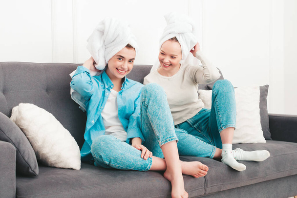 Two young beautiful smiling women sitting at the sofa. Sexy carefree models posing indoors in posh apartment or hotel room. They doing beauty treatments at home in towels on heads - Фото, изображение