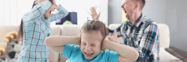 Kleines Mädchen verdeckt die Ohren mit den Händen vor dem Hintergrund fluchender Eltern zu Hause - Foto, Bild