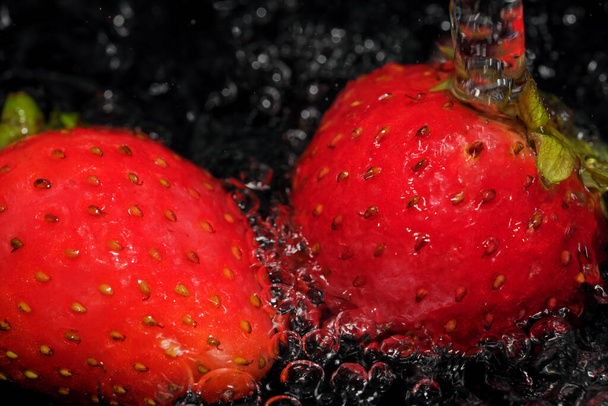 Rode rijpe aardbeien worden gewassen in schoon water close-up macro fotografie op een zwarte achtergrond - Foto, afbeelding