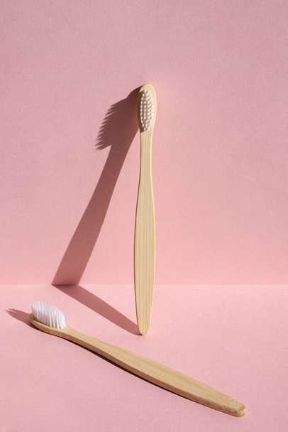Two eco friendly bamboo wooden toothbrushes on a pink background. Hard light. - Zdjęcie, obraz