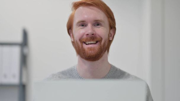 Barba pelirroja hombre con portátil sonriendo a la cámara - Foto, imagen