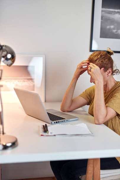 Женщина работает из дома на ноутбуке и у нее болит голова. - Фото, изображение