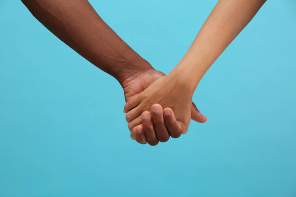 Woman and African American man holding hands on light blue background, closeup - Fotoğraf, Görsel