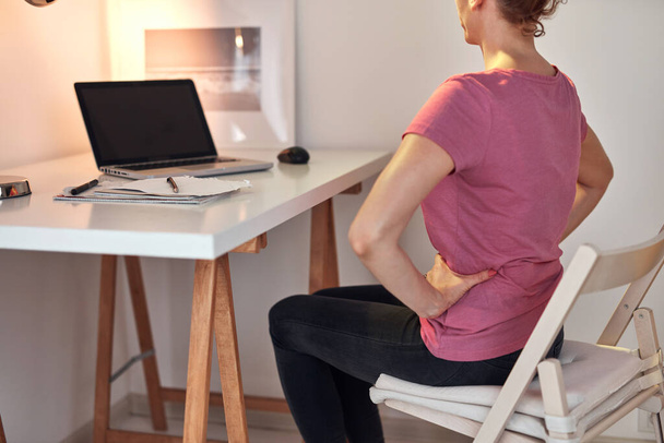 Femme travaillant sur un ordinateur portable à la maison et ayant des problèmes avec les hanches, le dos et les maux de ventre. - Photo, image