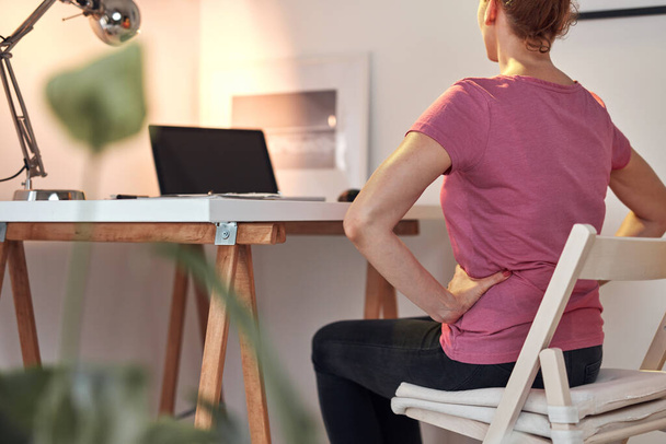 Woman working on a laptop at home and having problems with hips, back and stomack ache. - Foto, Bild