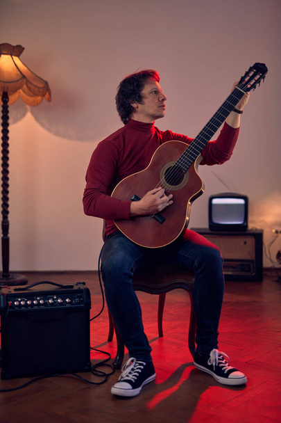 mężczyzna muzyk gra na gitarze akustycznej na wzmacniaczu w retro vintage pokój. - Zdjęcie, obraz
