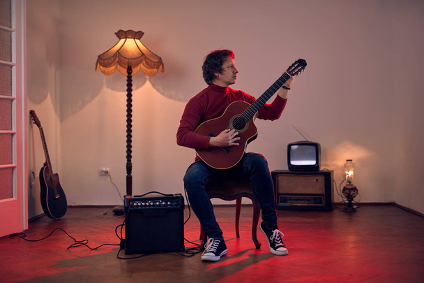 Mies muusikko soittaa akustista kitaraa vahvistimella retro vintage huoneessa. - Valokuva, kuva