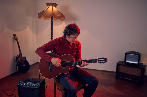 Mies muusikko soittaa akustista kitaraa vahvistimella retro vintage huoneessa. - Valokuva, kuva