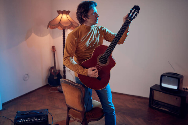 Männlicher Musiker spielt Akustikgitarre am Verstärker im Retro-Vintage-Raum. - Foto, Bild