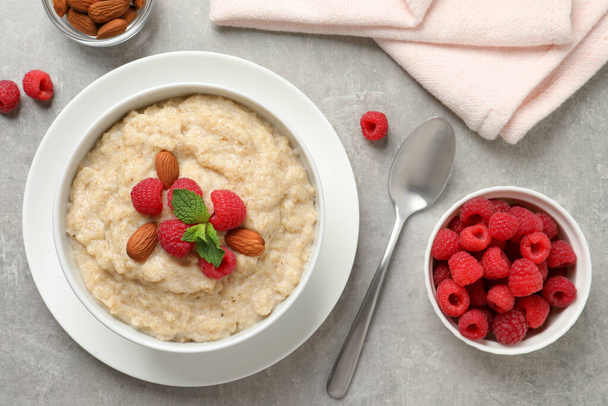Tasty oatmeal porridge with raspberries and almond nuts served on light grey table, flat lay - Foto, afbeelding