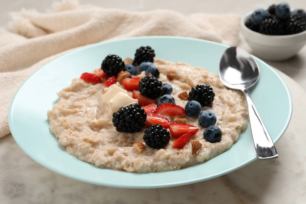 Tasty oatmeal porridge with berries and almond nuts in plate on table - Foto, afbeelding