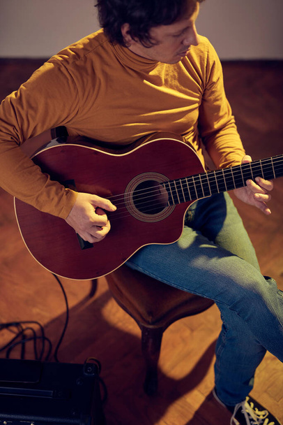 mężczyzna muzyk gra na gitarze akustycznej na wzmacniaczu w retro vintage pokój. - Zdjęcie, obraz