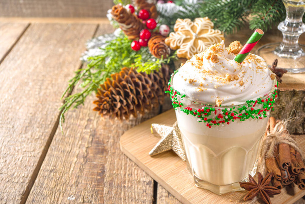 Праздничный рождественский напиток, коктейль из яичного коктейля с мороженым, взбитые сливки, красочные сахарные брызги, на деревянном традиционном фоне с рождественским декором и пряничным печеньем, пространство для копирования - Фото, изображение