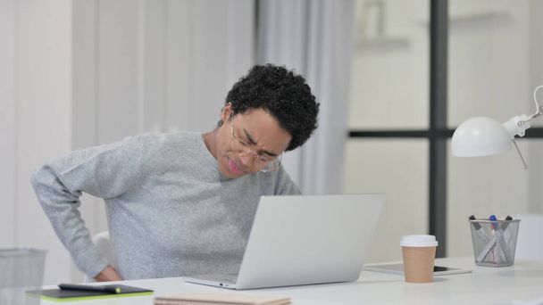 Afrikaanse vrouw met rugpijn tijdens het gebruik van laptop  - Foto, afbeelding
