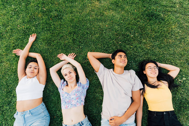 Grupa młodych wielonarodowych przyjaciół na świeżym powietrzu leżąca trawa uśmiechnięta i relaksująca - Zdjęcie, obraz