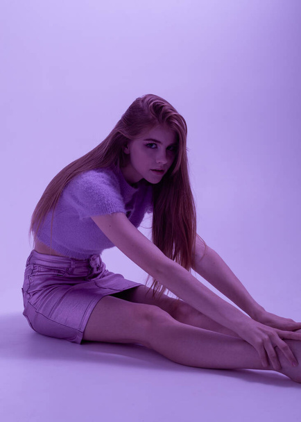 beautiful girl in fashionable, summer clothes in purple lighting sits on the floor - Fotó, kép