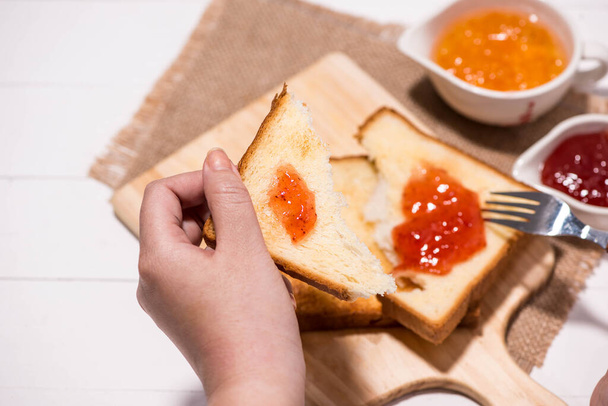 Vrouw handen eten brood met aardbei jam bij het ontbijt. Focus op handen. - Foto, afbeelding
