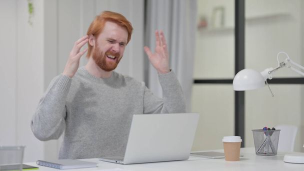 Бородатый рыженький реагирует на потерю во время работы на ноутбуке  - Фото, изображение