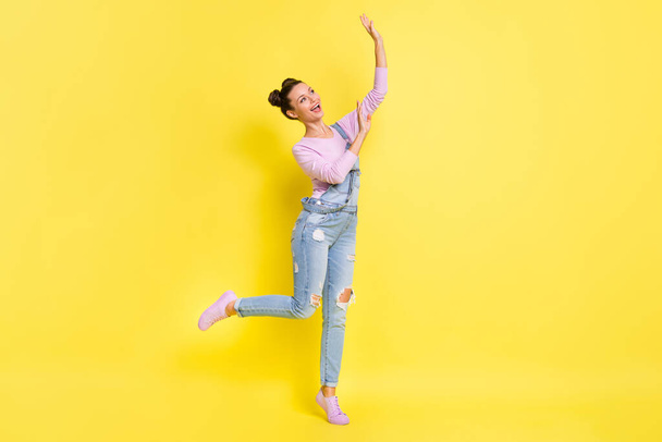 Photo of dreamy inspired lady stand tiptoe dance look empty space wear jeans overall sneakers isolated yellow background - 写真・画像