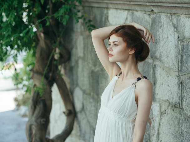 Woman in white dress near tree basing stone wall Greece - Foto, afbeelding