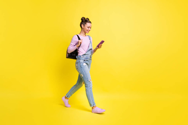 Full size profile photo of optimistic nice brunet lady go look telephone wear overall isolated on yellow background - 写真・画像