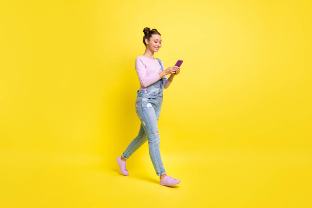 Full size profile photo of optimistic nice brunet lady go look telephone wear overall isolated on yellow background - Foto, afbeelding