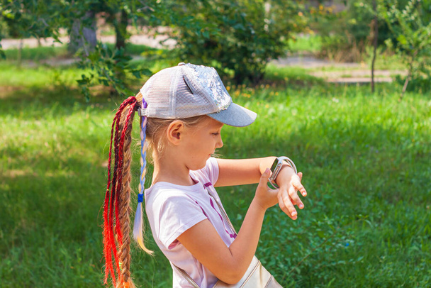 Lapsikoululainen käyttää älykelloa ulkona puistossa. Poika puhuu videopuhelussa vanhempiensa kanssa älykkäillä kelloilla. Koulutyttö etsii internetissä käyttäen kellot kosketusnäyttö näyttö.Smart rannekello GPS tracker - Valokuva, kuva
