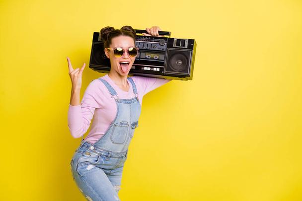 Photo of optimistic nice brunet lady tongue out hold boom box wear overall isolated on yellow background - Фото, зображення
