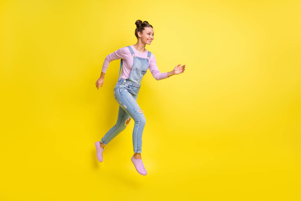 Profile photo of fast lady jump run look empty space wear denim overall shoes isolated yellow background - 写真・画像