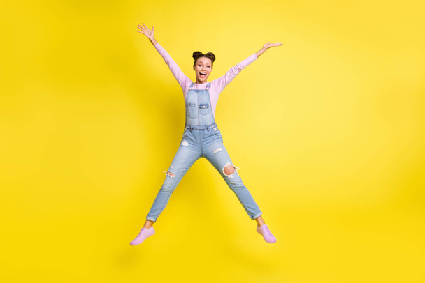 Photo of excited cute lady jump star shape raise hands open mouth wear jeans overall shoes isolated yellow background - Foto, afbeelding