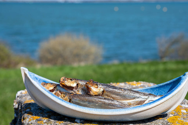 Gerookte sprattus of sprot zeevissen geserveerd buiten met uitzicht op blauw zeewater klaar om te eten - Foto, afbeelding