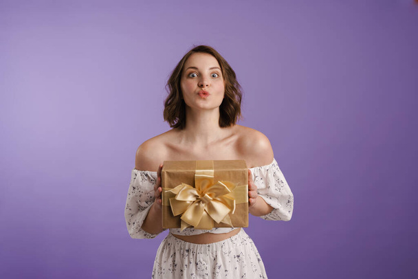 Joyeux jeune femme blanche tenant boîte cadeau sur fond violet - Photo, image