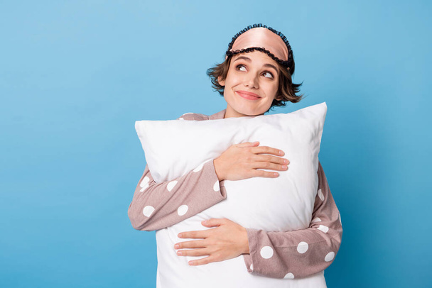 Photo of young attractive girl happy positive smile hug pillow bedtime dream look empty space isolated over blue color background - Фото, изображение