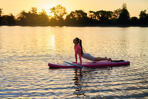 Vrouw stretching lichaam op sup board tijdens zonsondergang  - Foto, afbeelding