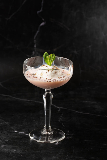 Glass of ice cold Baileys cocktail served in a glass, decorated with mint leaf placed on a black background - Photo, image