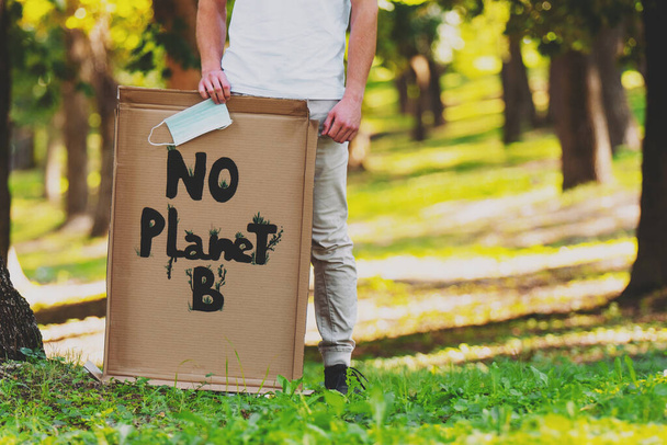 Αφίσα εκδήλωσης της αλλαγής του κλίματος Δεν Planet B κρατώντας από έναν άνθρωπο και κρατώντας στο χέρι του μια ιατρική μάσκα διαμαρτύρονται για να σώσει τον πλανήτη γη. - Φωτογραφία, εικόνα