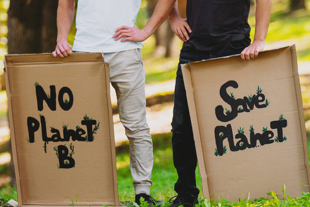 Cropped photo of two men in black and white clothes holding the cardboard posters with inscription to save our planet and protect it from the pollution. - Фото, изображение