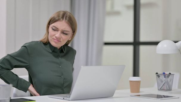 Mujer joven que tiene dolor de espalda mientras usa el ordenador portátil  - Foto, imagen