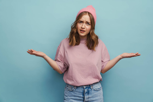 Young unhappy woman frowning and throwing hands aside isolated over blue background - Foto, Bild