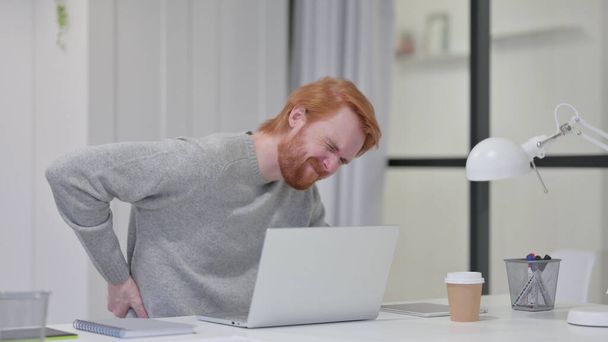 brodaty rudzielec mając ból pleców podczas pisania na laptopie  - Zdjęcie, obraz