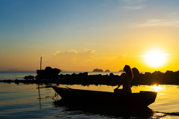 Romantic boat trip with a girl at sunset. The girl is sitting in a wooden boat on the ocean. - 写真・画像