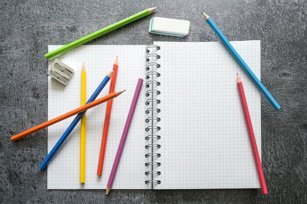 Flat lay of a blank open spiral notebook with copy space, colored crayons, sharpener and eraser for creative work, study or school on a gray table, high angle view, selected focus - Foto, Imagen