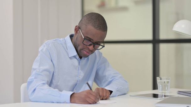 Afrikaanse man schrijft op papier aan het werk  - Foto, afbeelding