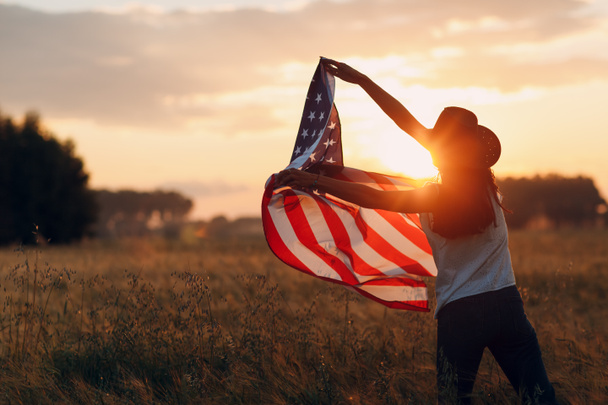 Woman farmer in the agricultural field with american flag on sunset - Photo, Image