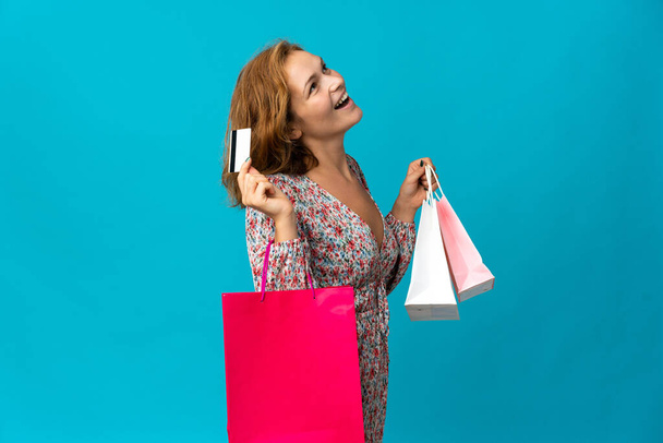 青の背景に隔離されたショッピングバッグを持つ若いグルジアの女性ショッピングバッグとクレジットカードを保持 - 写真・画像